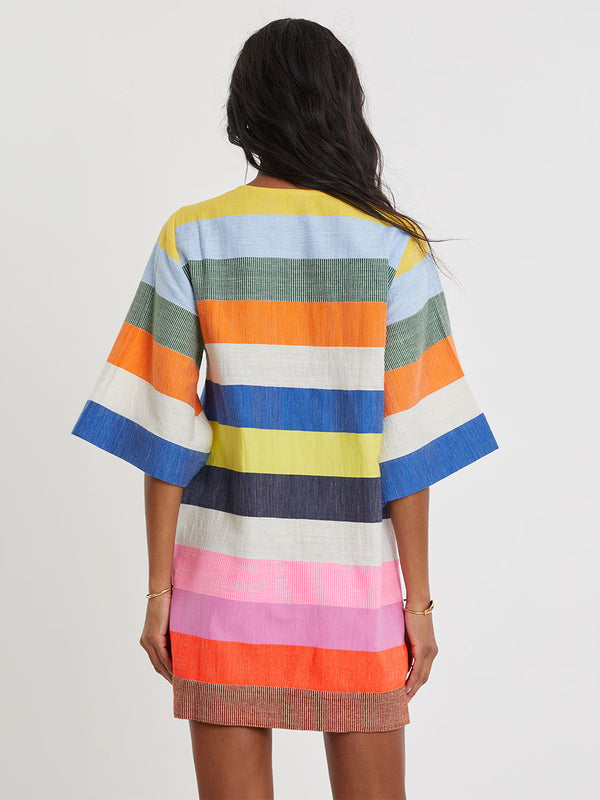 Woman wearing lemlem handwoven BELKIS Dress featuring bold, joyful stripe pattern in vibrant shades of blue, yellow, pink, orange, and green