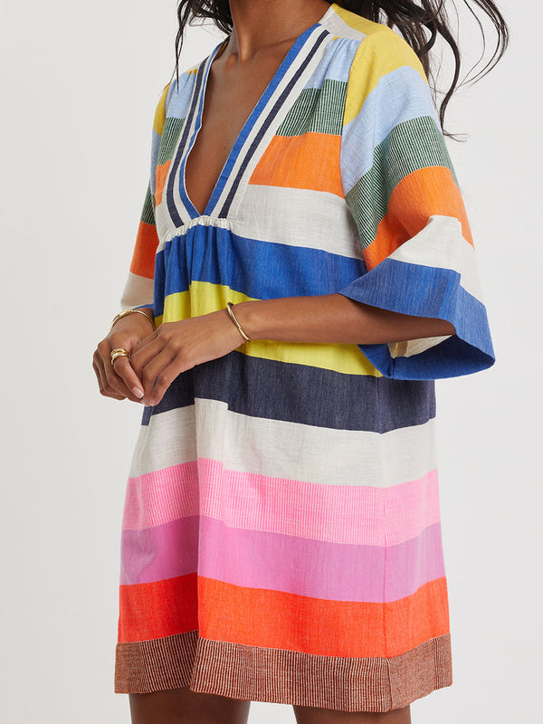 Woman wearing lemlem handwoven BELKIS Dress featuring bold, joyful stripe pattern in vibrant shades of blue, yellow, pink, orange, and green
