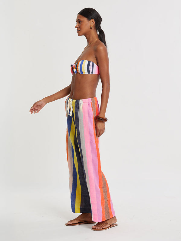 Woman wearing lemlem DESTA handwoven pants  featuring bold, joyful stripe pattern in vibrant shades of blue, yellow, pink, orange, and green