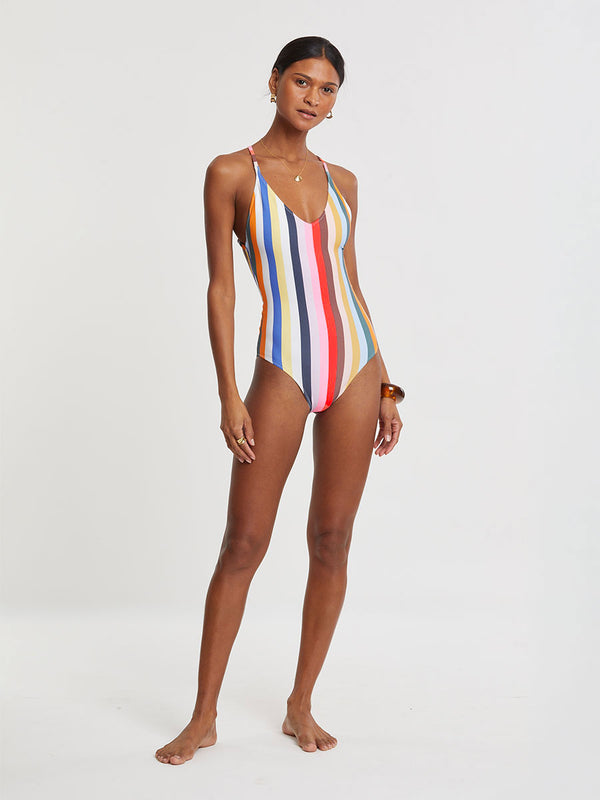 Woman wearing lemlem RETIRO One Piece featuring bold, joyful stripe pattern in vibrant shades of blue, yellow, pink, orange, and green