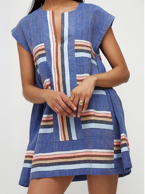 Woman standing wearing lemlem handwoven ELINA Caftan featuring navy, pink, beige, pale blue on a blue background.