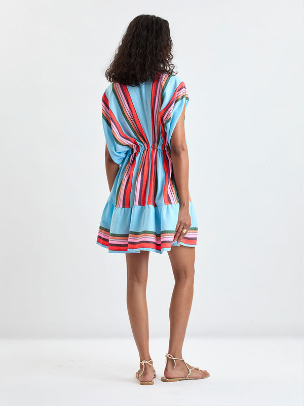 Back of a Woman wearing lemlem ALEM Dress featuring  bold stripes in soft pink, tangerine, scarlet, forest green, and burgundy, set against a light aqua background.
