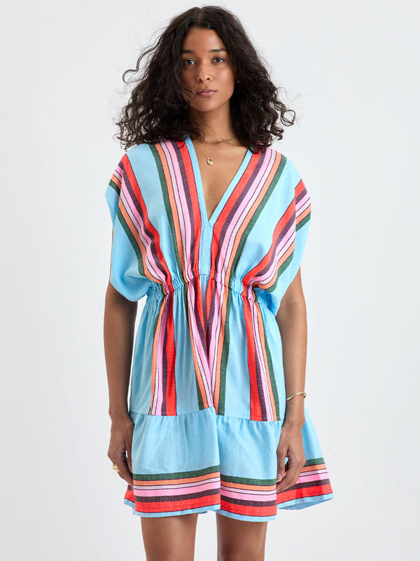 Woman wearing lemlem ALEM Dress featuring  bold stripes in soft pink, tangerine, scarlet, forest green, and burgundy, set against a light aqua background.