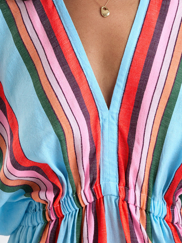 Close up on a Woman wearing lemlem ALEM Dress featuring  bold stripes in soft pink, tangerine, scarlet, forest green, and burgundy, set against a light aqua background.