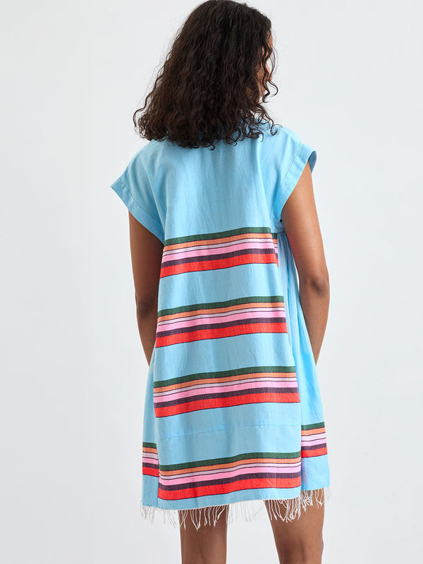 Back of a Woman wearing lemlem ELINA Caftan featuring  bold stripes in soft pink, tangerine, scarlet, forest green, and burgundy, set against a light aqua background.