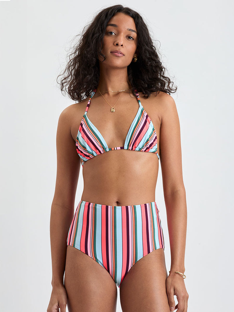 Woman wearing lemlem  MALIA Triangle top and ELSI High Waist Bottom featuring color block stripe pattern in white on sky blue background