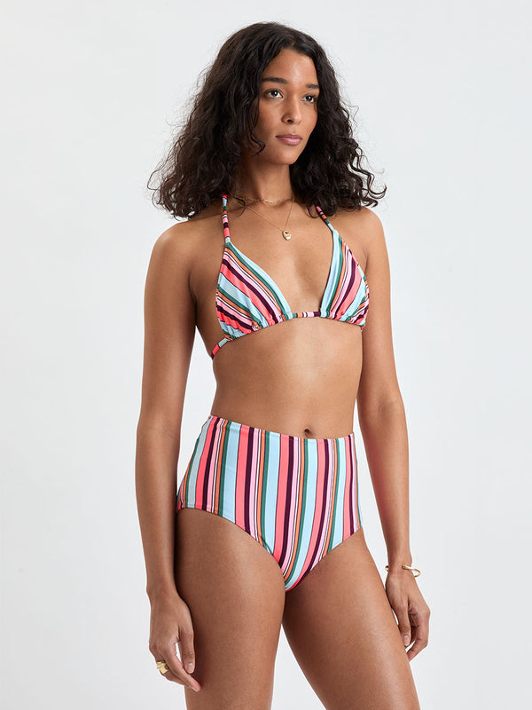 Woman wearing lemlem  MALIA Triangle top and ELSI High Waist Bottom featuring color block stripe pattern in white on sky blue background
