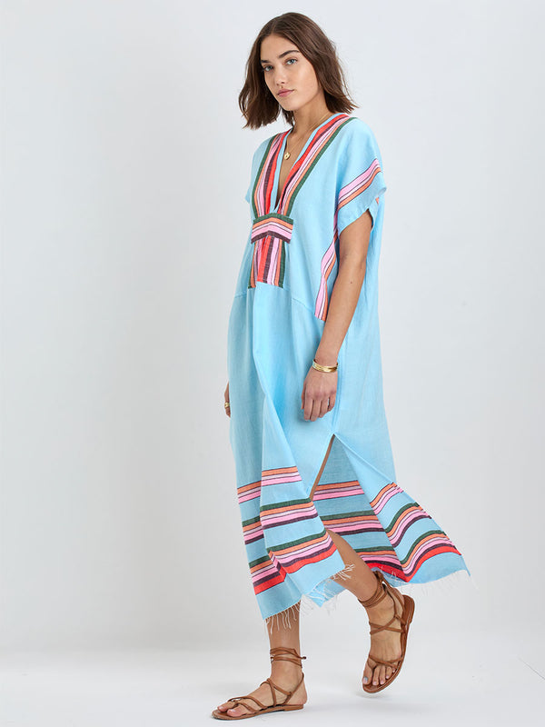 woman wearing lemlem GASIRA Caftan featuring  bold stripes in soft pink, tangerine, scarlet, forest green, and burgundy, set against a light aqua background.