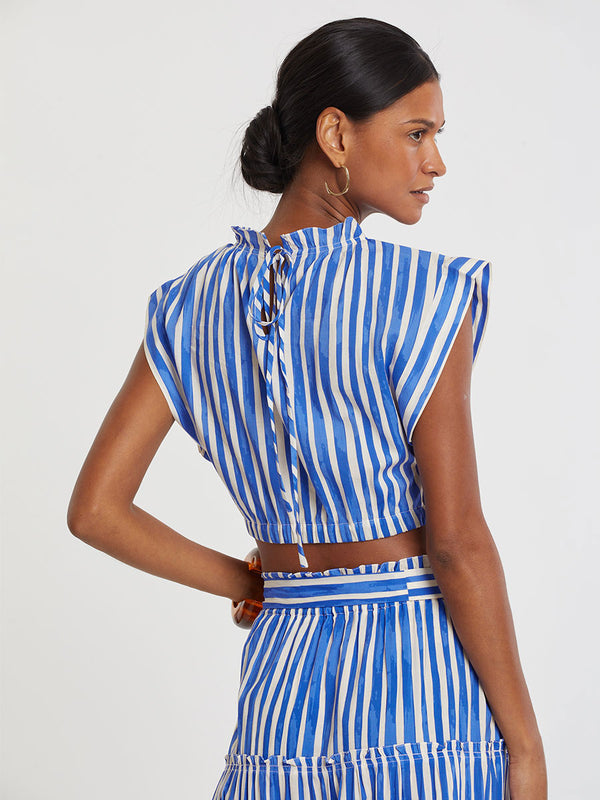 Woman standing wearing lemlem MUNA Ruched Crop Top and SANAA Skirt featuring an exclusive in-house designed painted-effect stripe print in a vibrant, dazzling blue on a white background