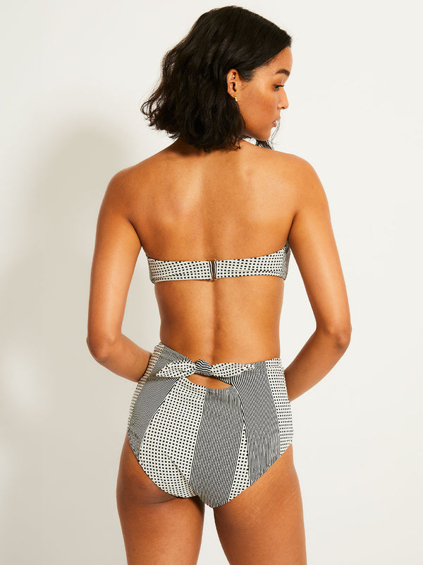 Back of a Woman Standing Wearing lemlem AVA Bandeau Top  featuring archive signature handwoven Semira patter in black and ivory colors and matching high waist bottom
