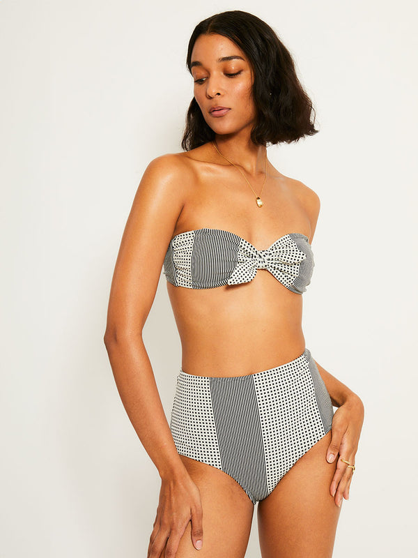 Woman Standing Wearing lemlem AVA Bandeau Top  featuring archive signature handwoven Semira patter in black and ivory colors and matching high waist bottom
