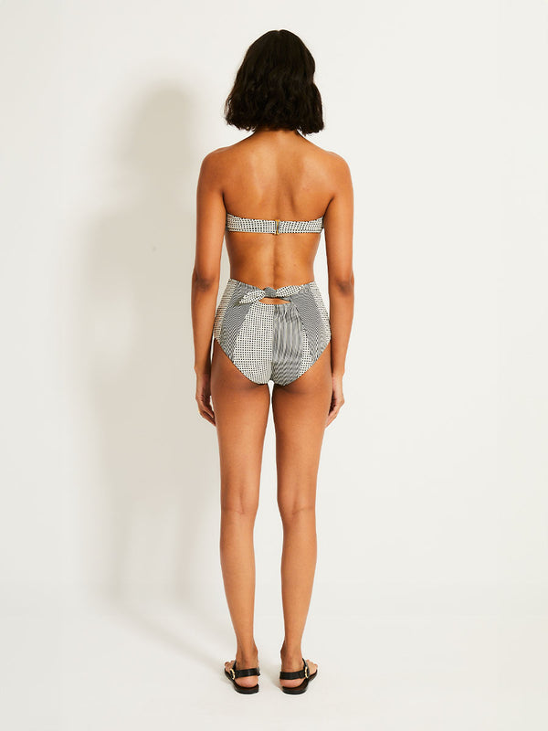 Back of a Woman Standing Wearing lemlem ELSI High Waist Bottom  featuring archive signature handwoven Semira patter in black and ivory colors and matching bandeau top
