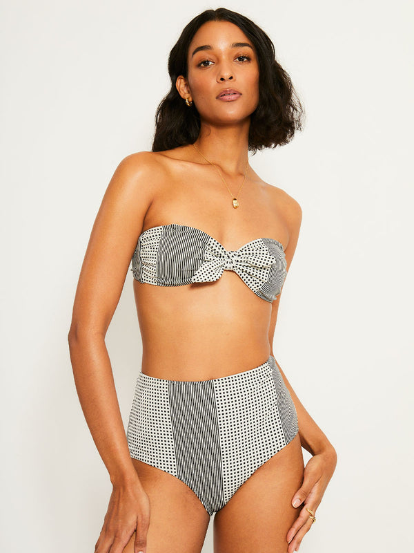 Woman Standing Wearing lemlem ELSI High Waist Bottom  featuring archive signature handwoven Semira patter in black and ivory colors and matching bandeau top
