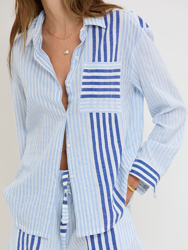 Woman Standing wearing lemlem  handwoven AISHA Shirt and SAFIA Shorts featuring  layered stripe pattern combining crisp deep-blue lines with softer, washed sky-blue stripes and MALIA Triangle Top.