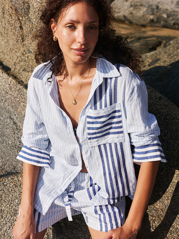 Woman wearing a blue and white striped lemlem handwoven AISHA Shirt and SAFIA Shorts sitting against a stone wall.