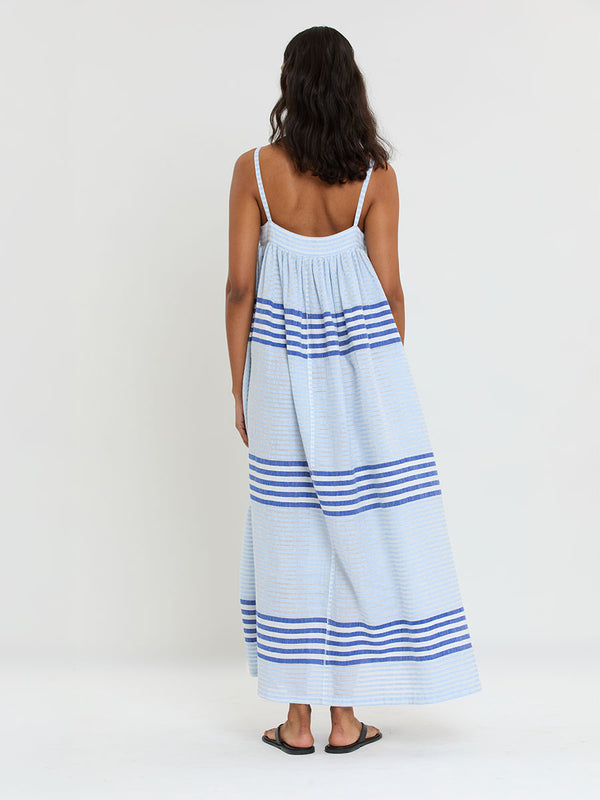 Woman Standing wearing lemlem  handwoven EDA Slip Dress featuring  layered stripe pattern combining crisp deep-blue lines with softer, washed sky-blue stripes and MALIA Triangle Top.
