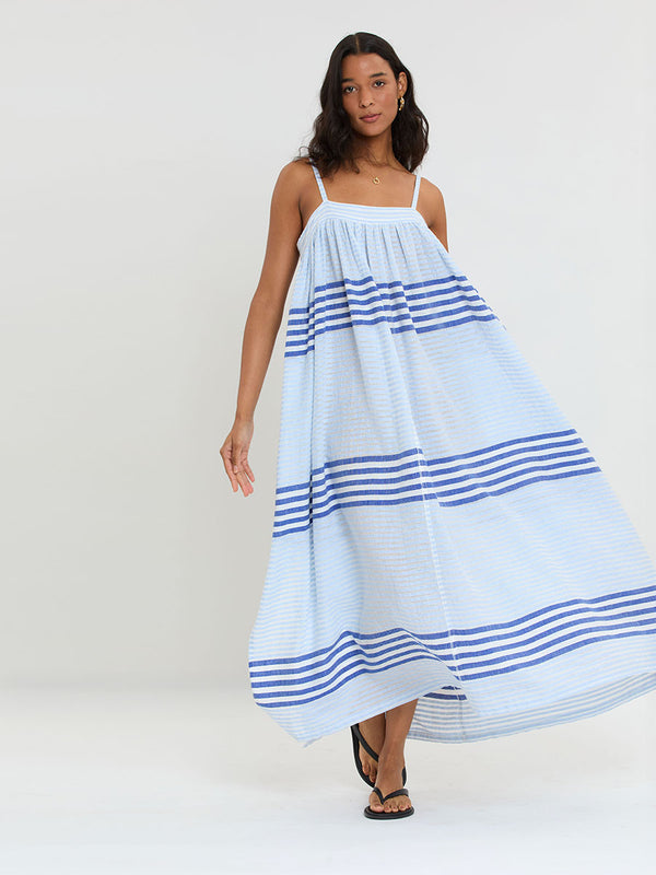 Woman Standing wearing lemlem  handwoven EDA Slip Dress featuring  layered stripe pattern combining crisp deep-blue lines with softer, washed sky-blue stripes and MALIA Triangle Top.