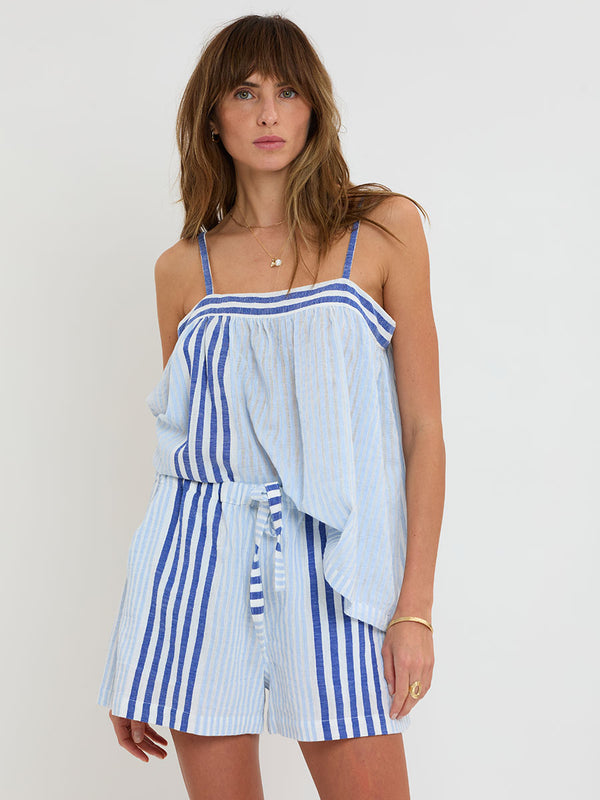 Woman Standing wearing lemlem  handwoven THEA Top and SAFIA Shorts featuring  layered stripe pattern combining crisp deep-blue lines with softer, washed sky-blue stripes.