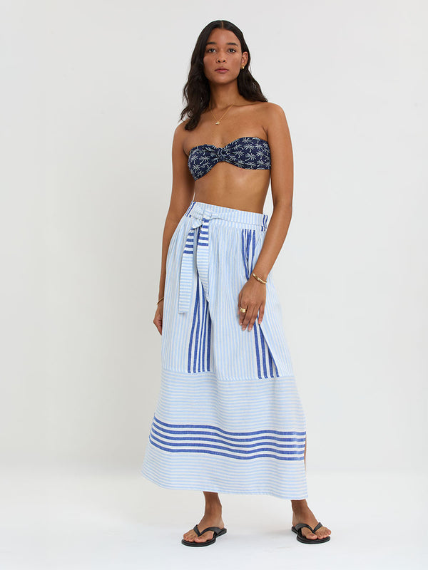 Woman Standing wearing lemlem  handwoven TOLA Skirt featuring  layered stripe pattern combining crisp deep-blue lines with softer, washed sky-blue stripes and AVA Bandeau Top.