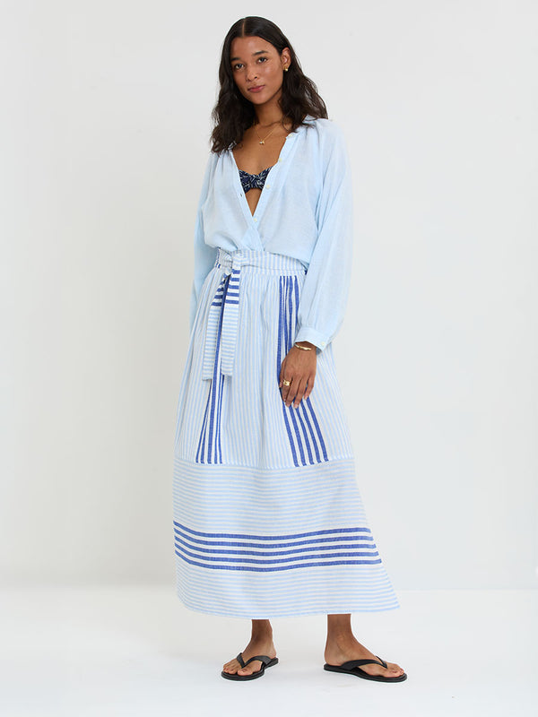 Woman Standing wearing lemlem  handwoven TOLA Skirt featuring  layered stripe pattern combining crisp deep-blue lines with softer, washed sky-blue stripes and MITA Blouse in Sky Blue