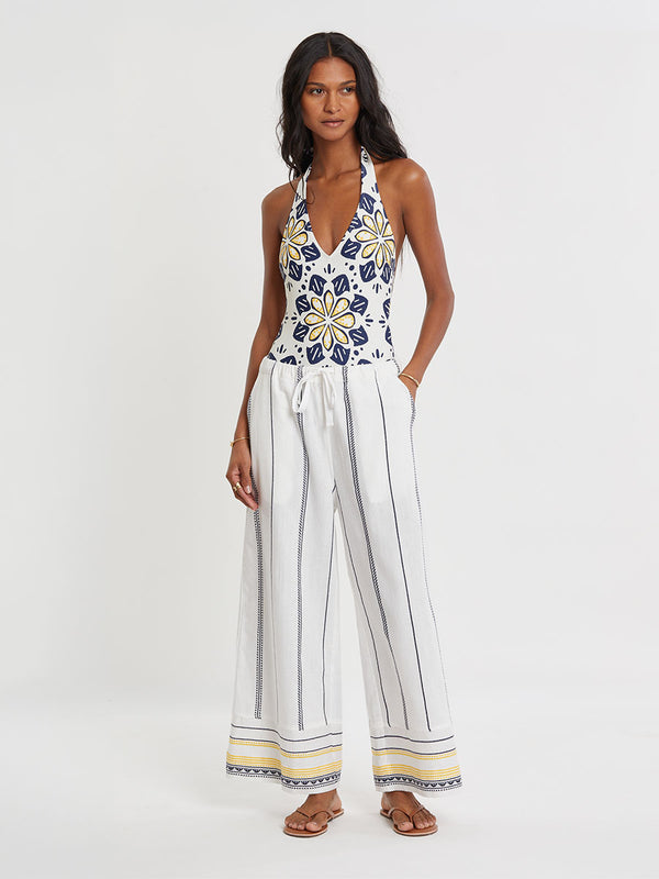Woman wearing lemlem handwoven DESTA Pants  featuring an intricate tibeb scallop pattern in navy, accented with yellow on a white background.