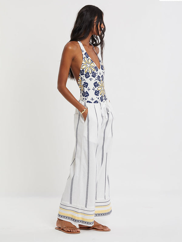 Woman wearing lemlem handwoven DESTA Pants  featuring an intricate tibeb scallop pattern in navy, accented with yellow on a white background.