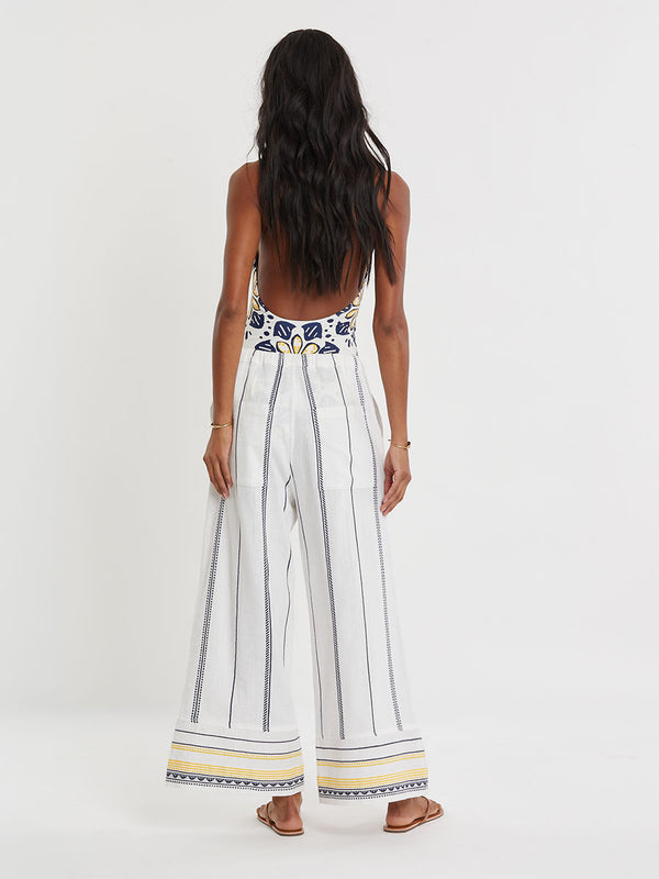 Woman wearing lemlem handwoven DESTA Pants  featuring an intricate tibeb scallop pattern in navy, accented with yellow on a white background.
