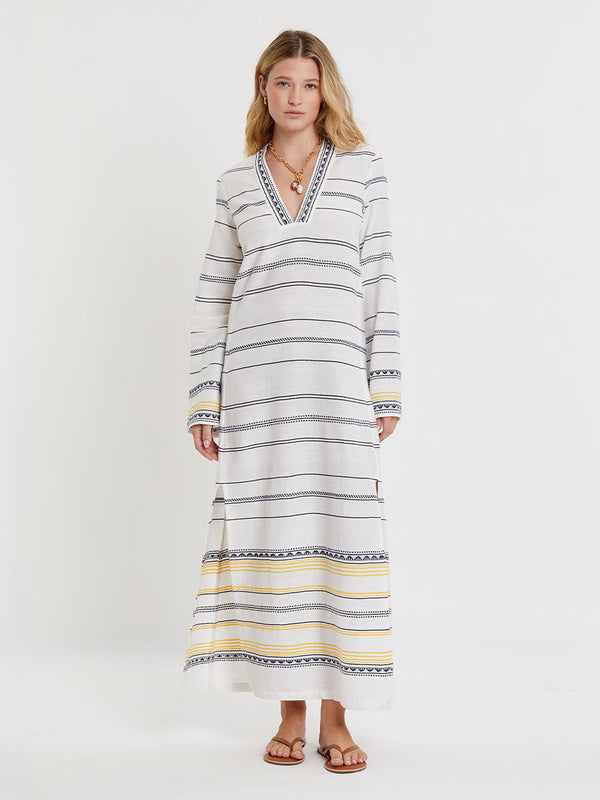 Woman wearing lemlem handwoven THEODORA Dress featuring an intricate tibeb scallop pattern in navy, accented with yellow on a white background.