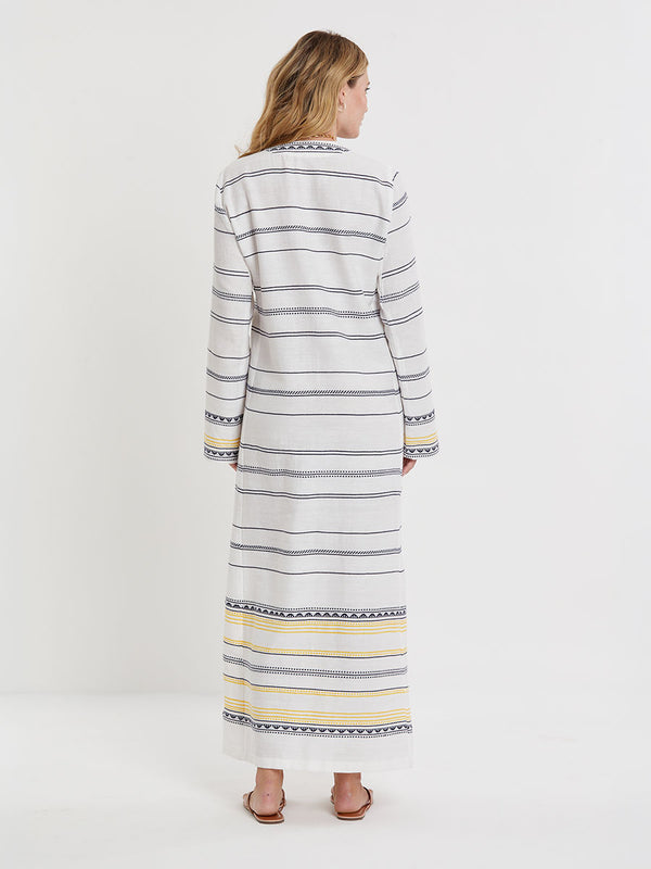 Woman wearing lemlem handwoven THEODORA Dress featuring an intricate tibeb scallop pattern in navy, accented with yellow on a white background.
