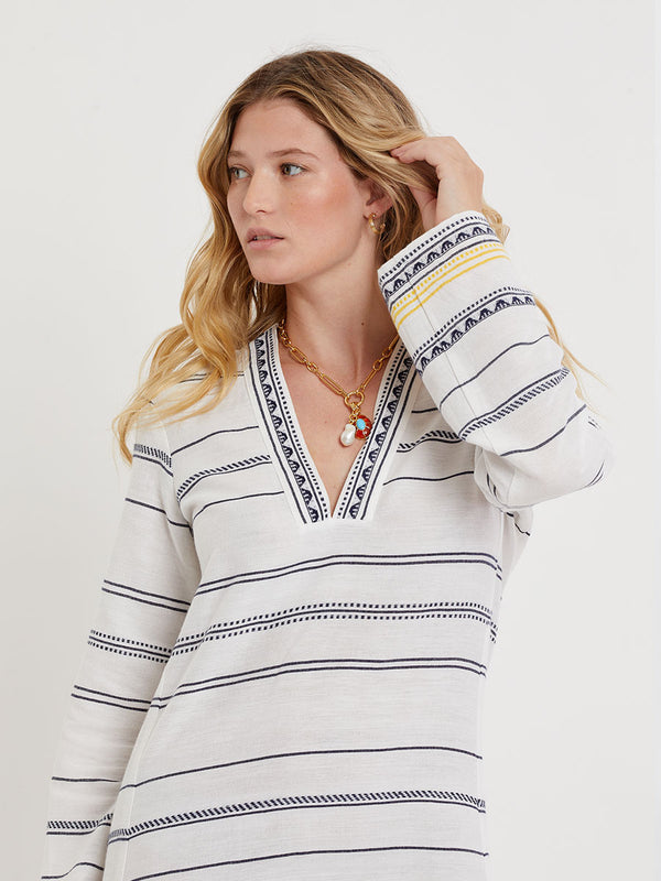 Woman wearing lemlem handwoven THEODORA Dress featuring an intricate tibeb scallop pattern in navy, accented with yellow on a white background.