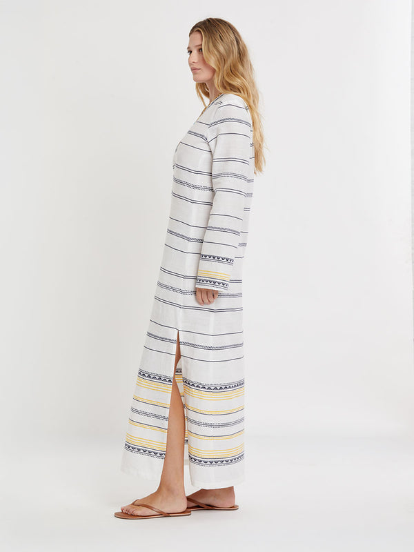 Woman wearing lemlem handwoven THEODORA Dress featuring an intricate tibeb scallop pattern in navy, accented with yellow on a white background.