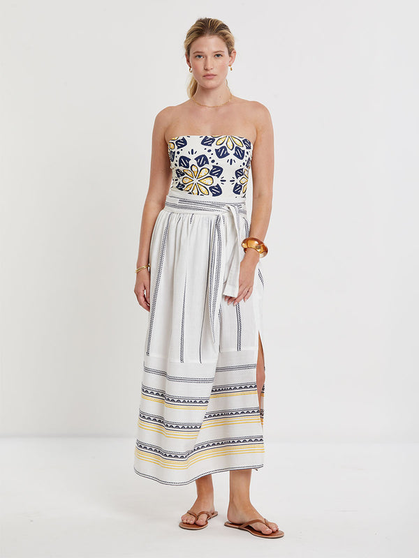 Woman wearing lemlem handwoven TOLA Skirt featuring an intricate tibeb scallop pattern in navy, accented with yellow on a white background.