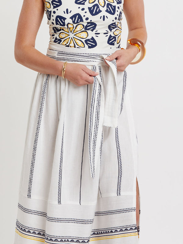 Woman wearing lemlem handwoven TOLA Skirt featuring an intricate tibeb scallop pattern in navy, accented with yellow on a white background.