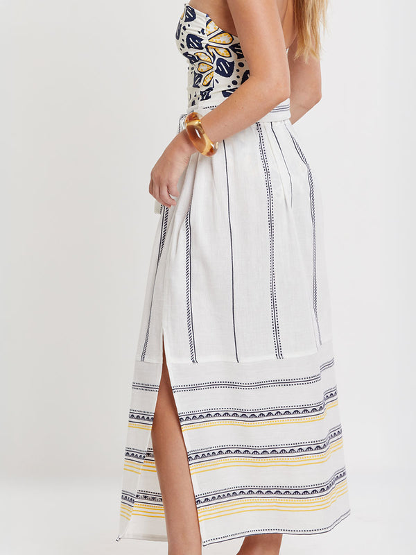 Woman wearing lemlem handwoven TOLA Skirt featuring an intricate tibeb scallop pattern in navy, accented with yellow on a white background.
