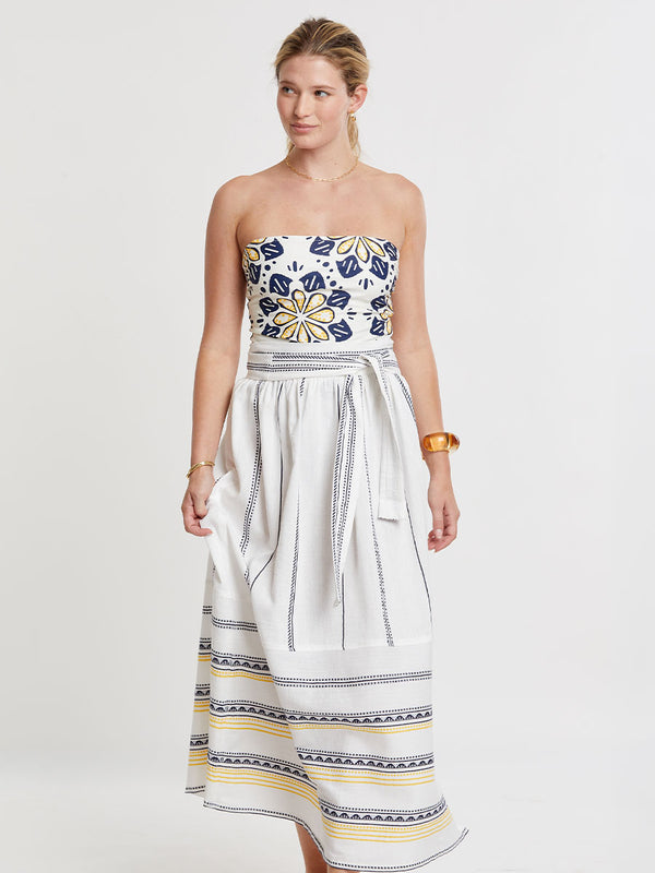Woman wearing lemlem handwoven TOLA Skirt featuring an intricate tibeb scallop pattern in navy, accented with yellow on a white background.