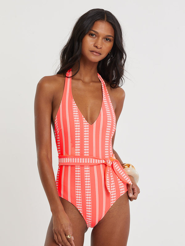 Woman Standing wearing lemlem LIDYA One Piece featuring intricate ivory Tibeb pattern on a bright coral pink background.