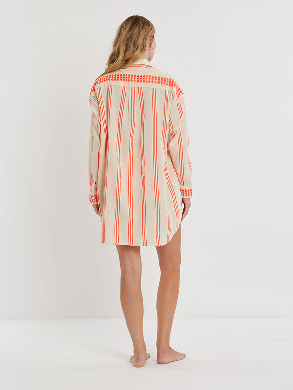 Woman Standing wearing lemlem handwoven MARIAM Shirt featuring intricate electric orange toned Tibeb pattern on a cream biscuit background.