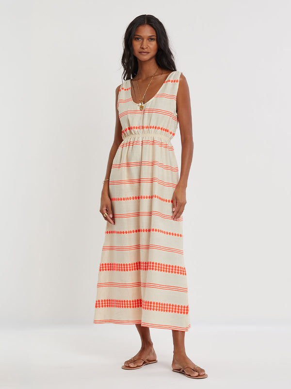 Woman Standing wearing lemlem handwoven MELAT Dress featuring intricate electric orange toned Tibeb pattern on a cream biscuit background.