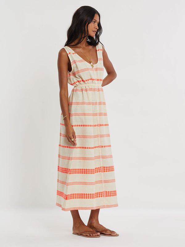 Woman Standing wearing lemlem handwoven MELAT Dress featuring intricate electric orange toned Tibeb pattern on a cream biscuit background.