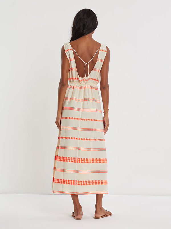 Woman Standing wearing lemlem handwoven MELAT Dress featuring intricate electric orange toned Tibeb pattern on a cream biscuit background.