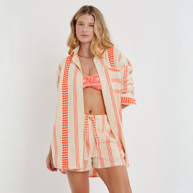 Woman wearing a matching set of MRIAM Shirt, AVA Bandeau Top , and SAFIA  shorts with red and white pattern on a light gray background