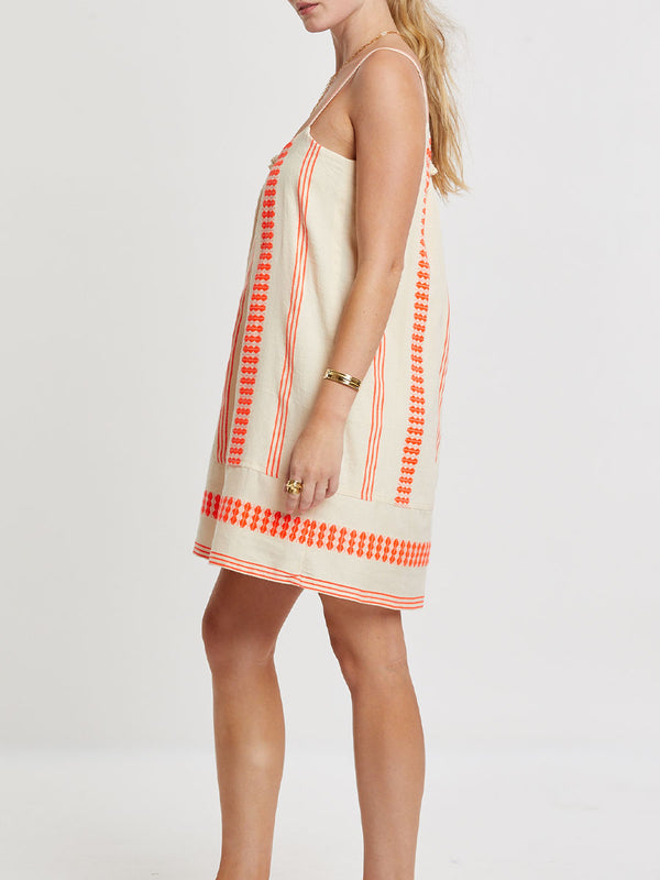 Woman Standing wearing lemlem handwoven ZINA Swing Dress featuring intricate electric orange toned Tibeb pattern on a cream biscuit background.