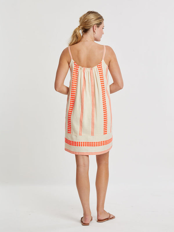 Woman Standing wearing lemlem handwoven ZINA Swing Dress featuring intricate electric orange toned Tibeb pattern on a cream biscuit background.