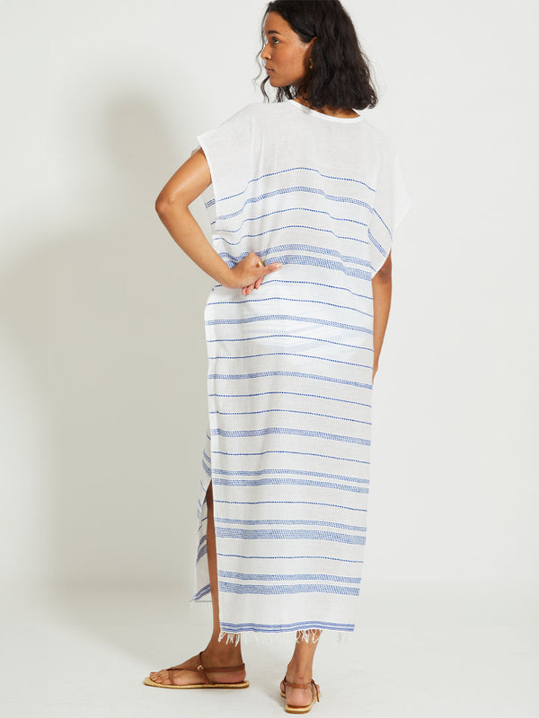 Back of a Woman Standing Wearing lemlem DALILA | V Neck Caftan featuring crisp white fabric woven with diagonal dotted stripes in bright blue and a subtle textured weave