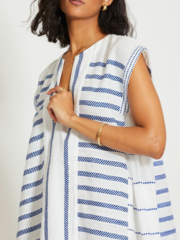 Close up on a Woman Standing Wearing lemlem ELINA | Caftan featuring crisp white fabric woven with diagonal dotted stripes in bright blue and a subtle textured weave