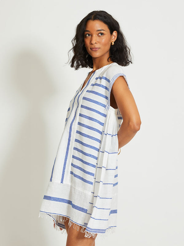 Woman Standing Wearing lemlem ELINA | Caftan featuring crisp white fabric woven with diagonal dotted stripes in bright blue and a subtle textured weave