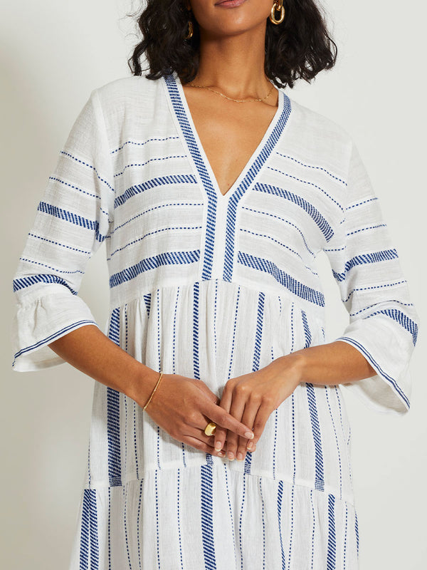 Close up on a Woman Standing Wearing lemlem HAWI | Flutter Dress featuring crisp white fabric woven with diagonal dotted stripes in bright blue and a subtle textured weave
