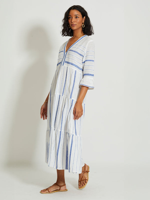 Woman Walking Wearing lemlem HAWI | Flutter Dress featuring crisp white fabric woven with diagonal dotted stripes in bright blue and a subtle textured weave