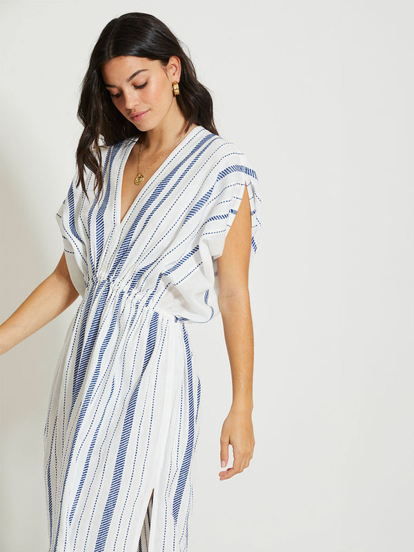 Woman Standing Wearing lemlem LEILA | Plunge Dress featuring crisp white fabric woven with diagonal dotted stripes in bright blue and a subtle textured weave