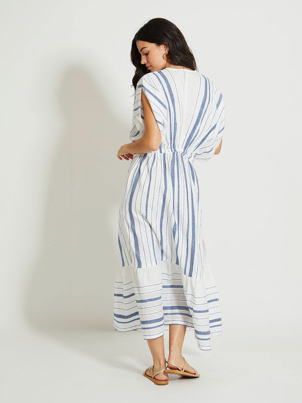 Back of a Woman Standing Wearing lemlem LEILA | Plunge Dress featuring crisp white fabric woven with diagonal dotted stripes in bright blue and a subtle textured weave